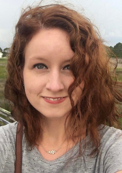 Head shot of Alexis smiling at the camera with her hair in her eyes