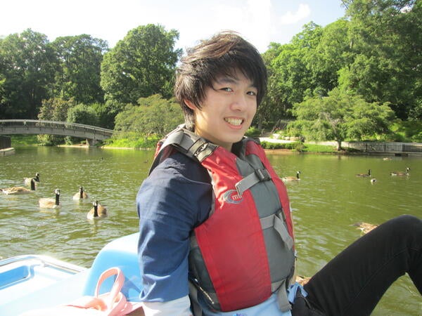 A young man looks to his right and smiles while sitting in a boat on a lake